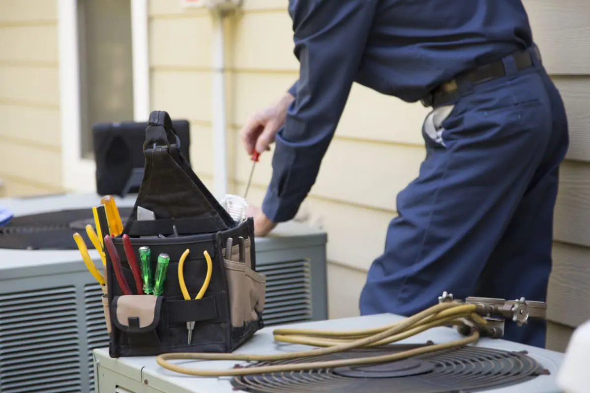 A technician’s tool bag and refrigerant gauge hoses on an outdoor condenser unit.